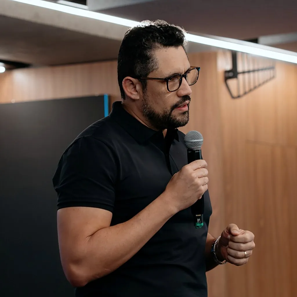 Vagner Campos de perfil, ao microfone, explicando com o punho fechado durante a aula