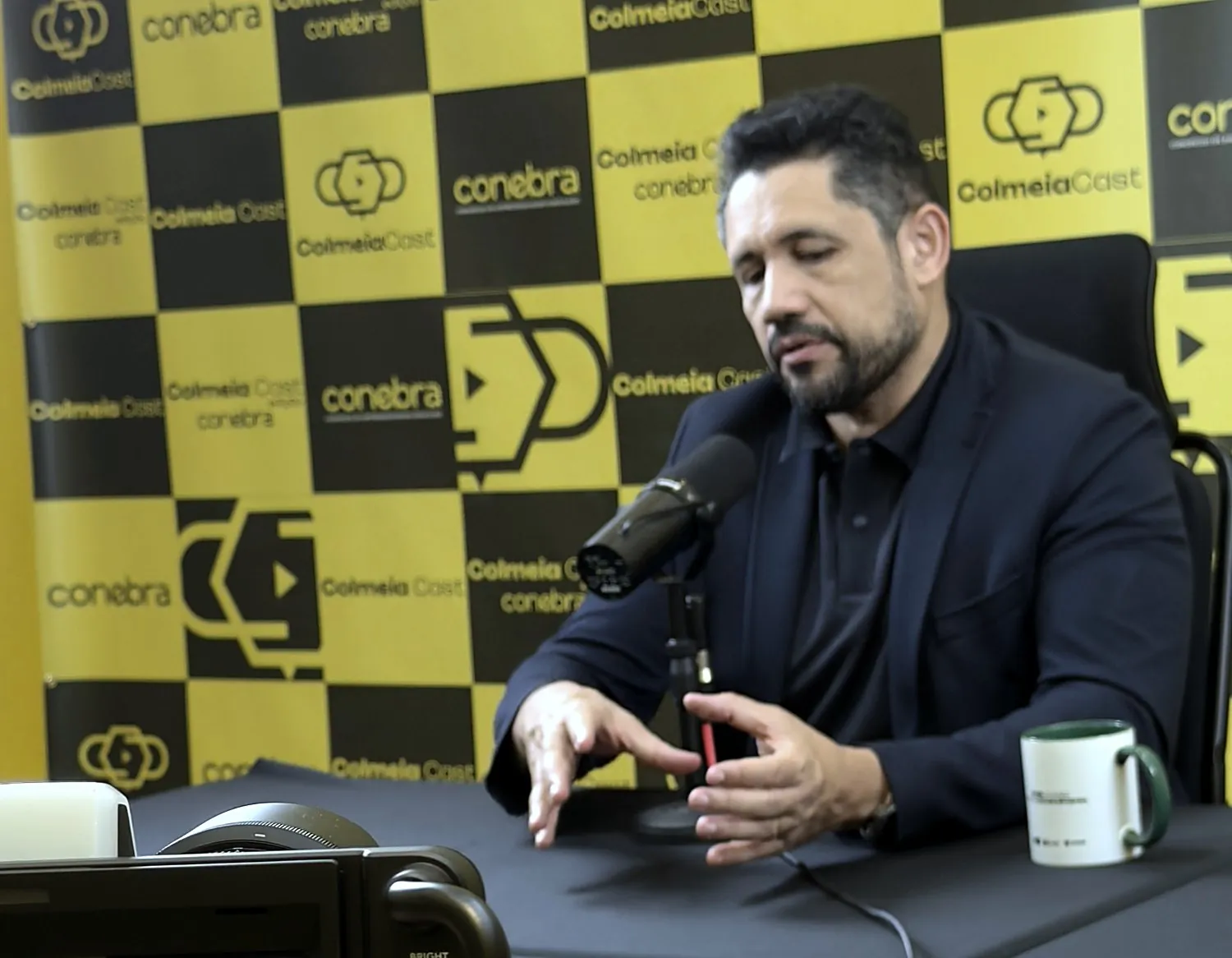 Vagner Campos falando ao microfone no ColmeiaCast, edição CONEBRA