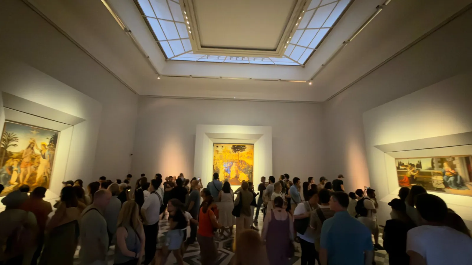 Sala de Leonardo da Vinci na Galleria degli Uffizi, em Florença, cheia de visitantes diante de três pinturas