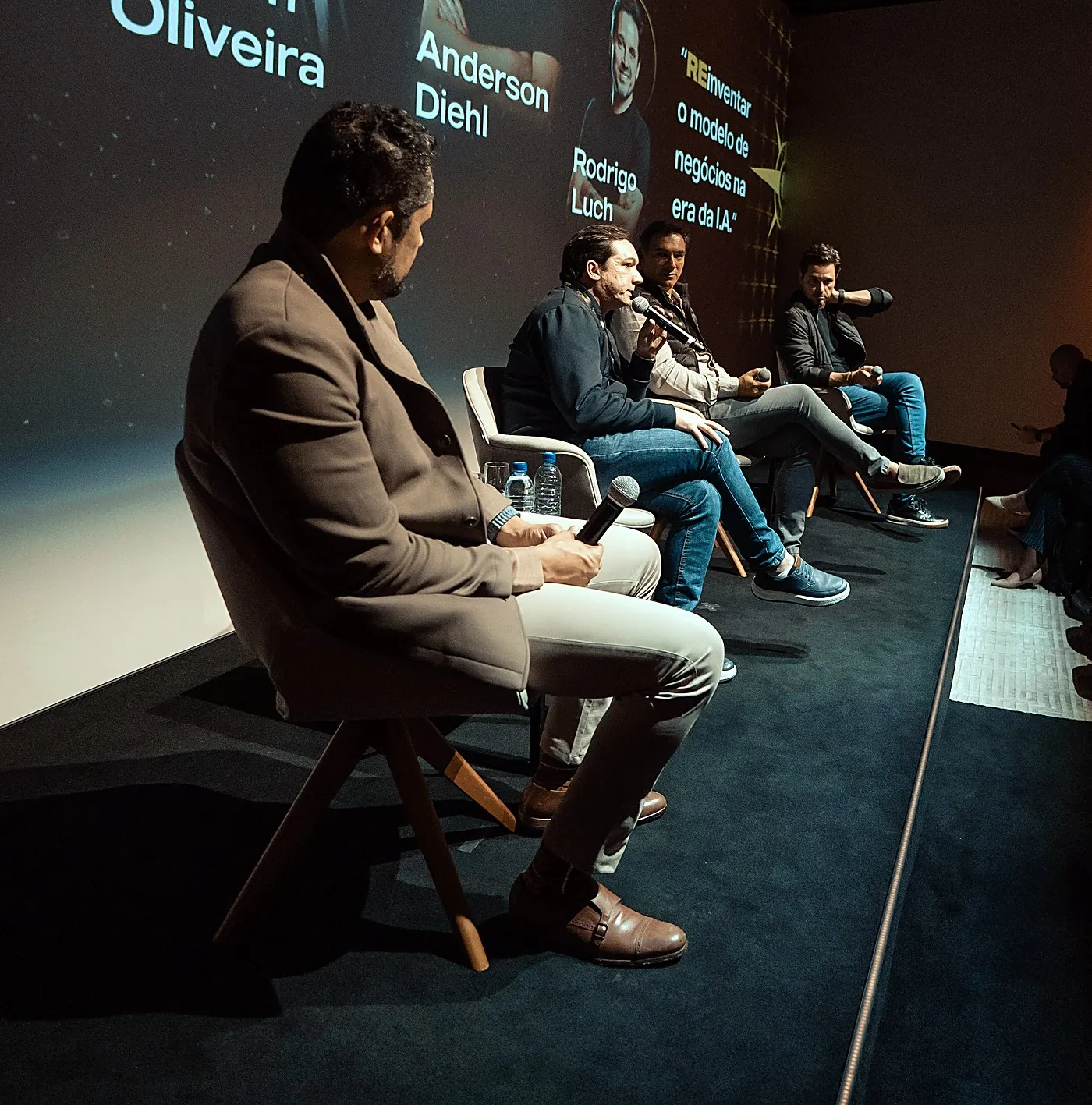 Vagner Campos em primeiro plano no palco, ouvindo os demais participantes do painel sobre reinventar o modelo de negócios na era da IA