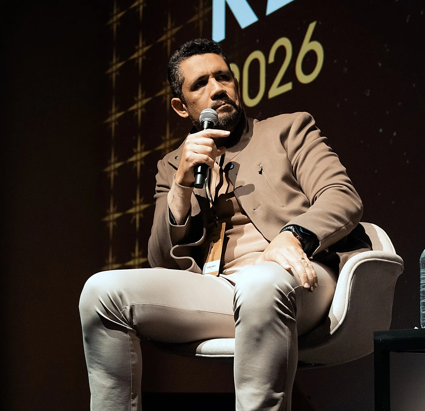 Vagner Campos sentado no palco, ao microfone, durante painel sobre IA nativa em ecossistema SaaS