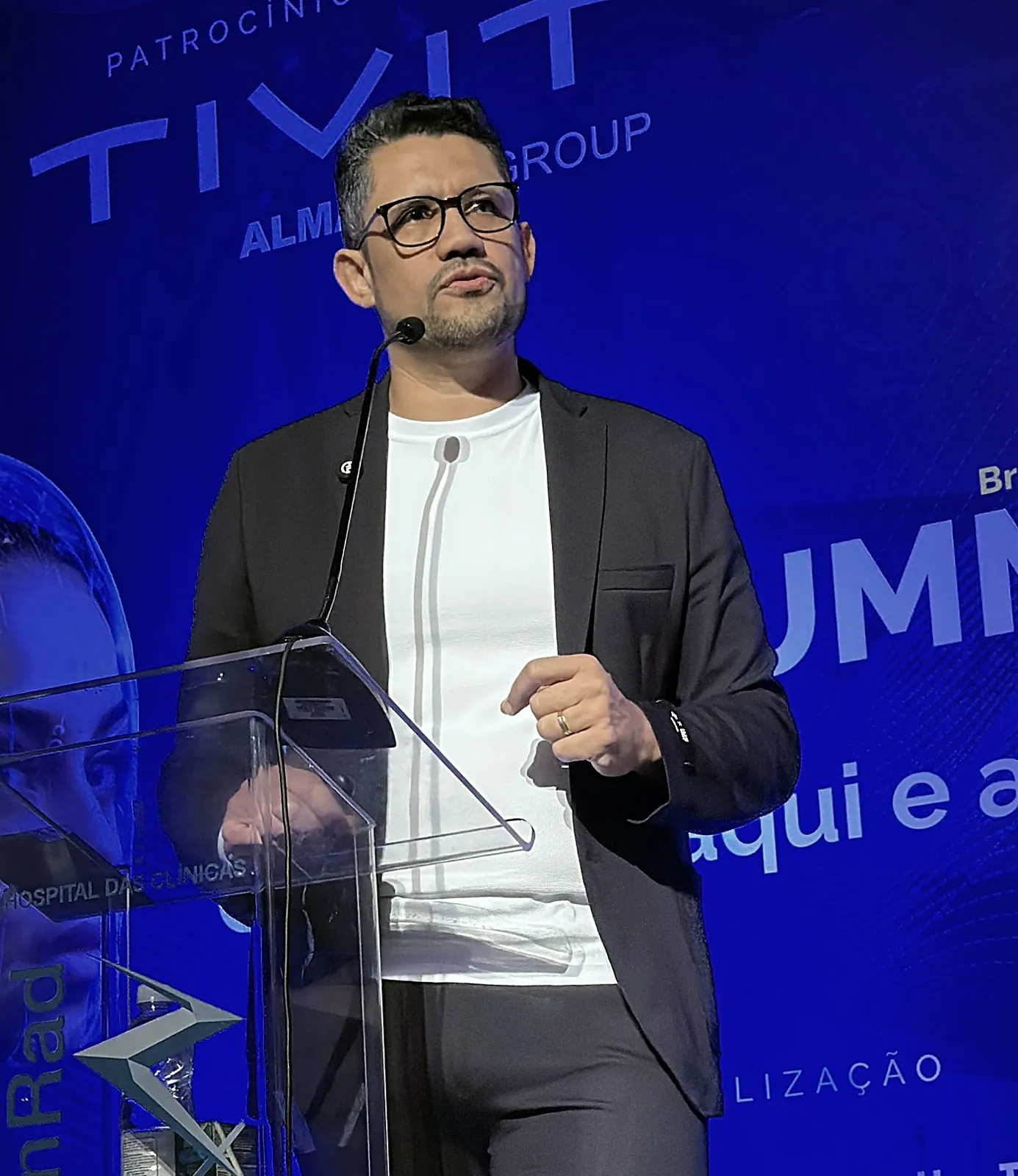 Vagner Campos ao púlpito do AI Summit Brasil 2025, diante do painel azul do evento