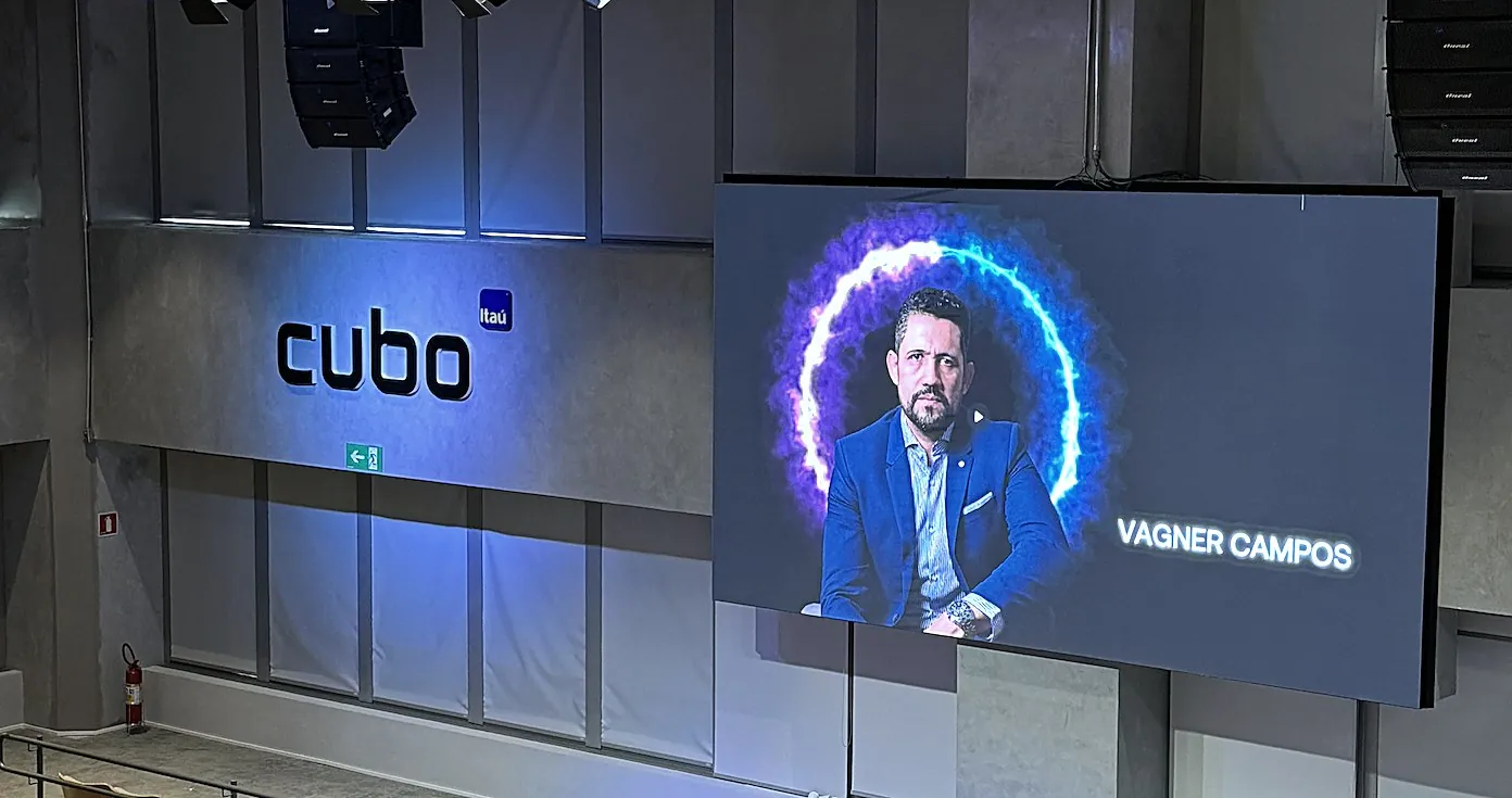 Telão do auditório do Cubo Itaú com a imagem e o nome de Vagner Campos na abertura de uma palestra