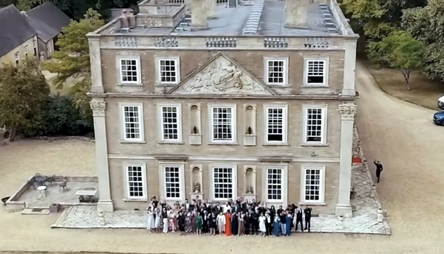 Vista aérea da Hinwick House, no Reino Unido, com o grupo de participantes do Secret Experience reunido diante da fachada