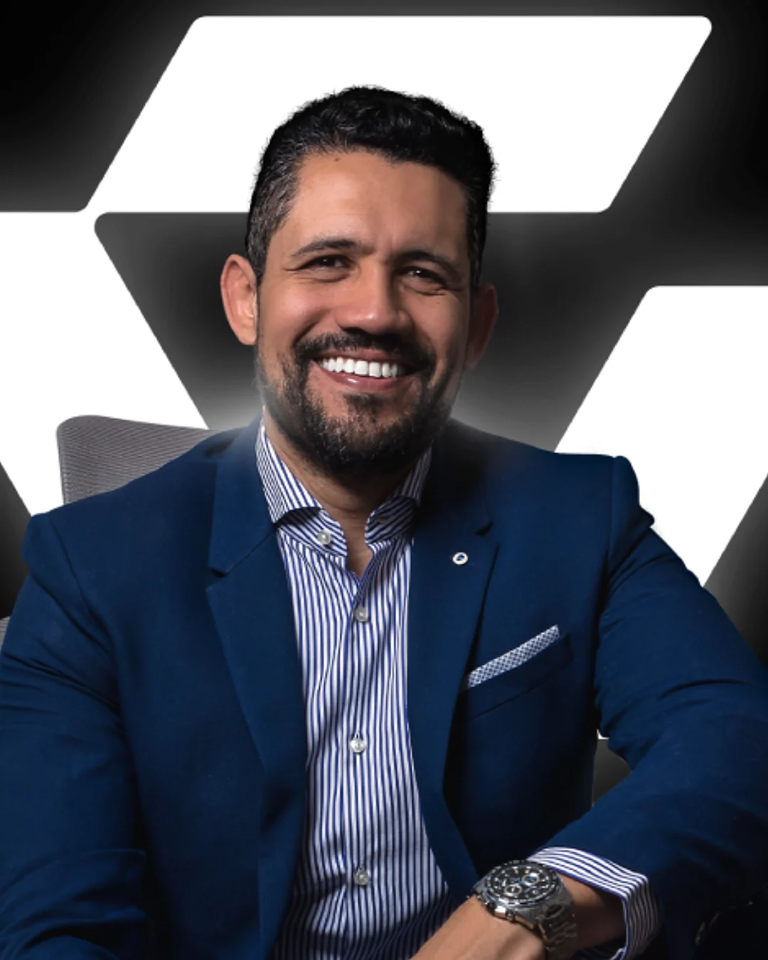 Vagner Campos sentado, sorrindo, diante do símbolo da sua marca pessoal