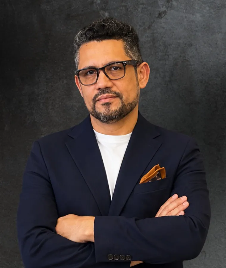 Vagner Campos de braços cruzados, de óculos e blazer azul-marinho, diante de um fundo escuro